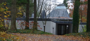 Front Entry: The street-facing side of the house is un-revealing, set back beyond a small wooded rise. The entry is set in a deep recess; there are no street-facing windows. The shape of the lead-coated copper roof predominates.